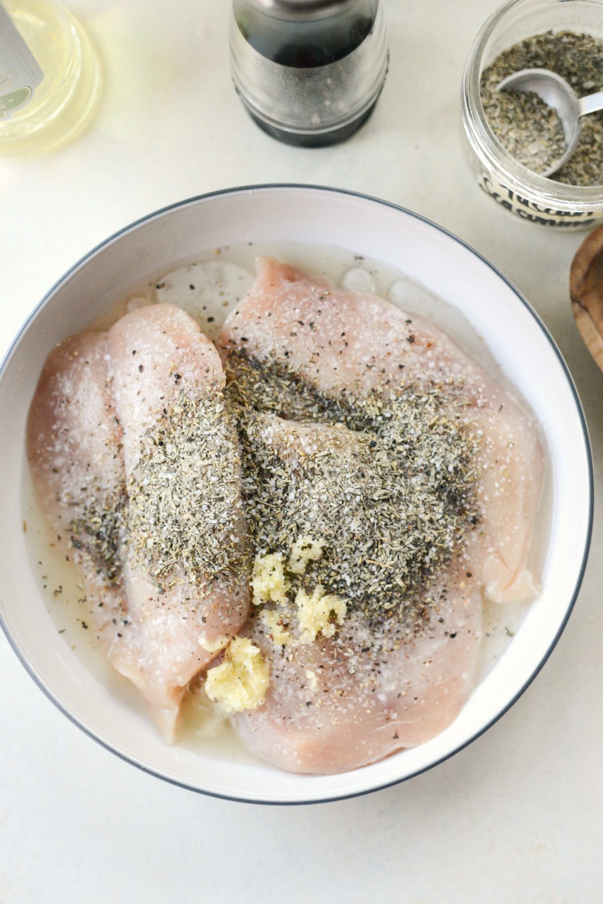 chicken in a bowl with oil, lemon juice, garlic and dried herbs