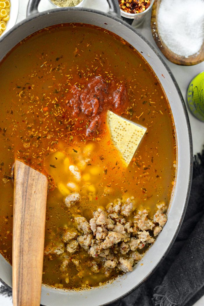 pour in broth, crushed tomatoes, beans, browned sausage and parmesan rind